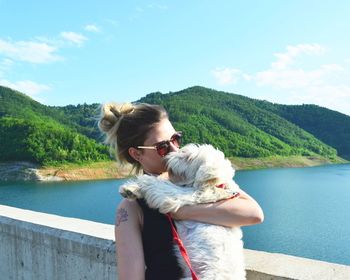 Young woman kissing dog while standing against river