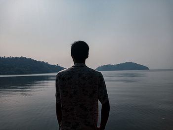 Rear view of man looking at sea against clear sky