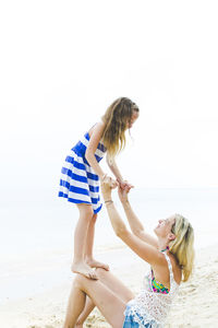 Girl standing on knees of mother at beach