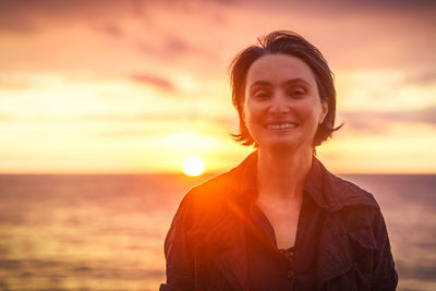 Portrait of smiling woman standing against sea and sky during sunset