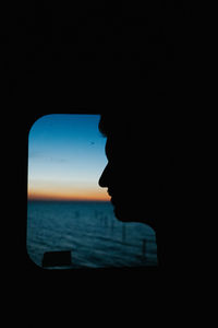 Silhouette man looking at sea seen through window