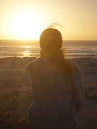 Rear view of woman standing on beach during sunset