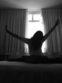 Rear view of woman stretching on bed at home