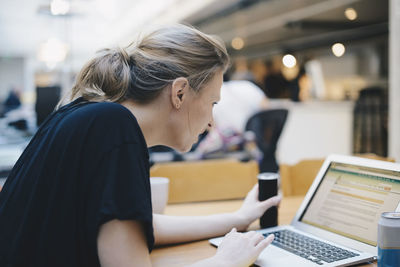 Side view of young female computer programmer using laptop at desk in office