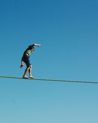 Low angle view of man skateboarding against clear blue sky