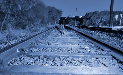 Rear view of man walking on railroad tracks during sunset