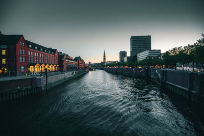 Illuminated bridge over river by buildings against sky in city