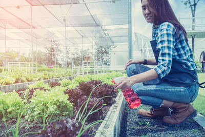 Side view of woman holding umbrella while sitting by plants