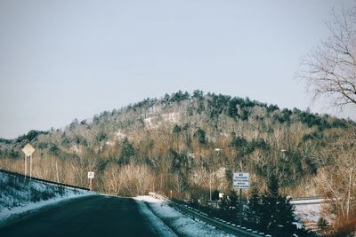 Road amidst trees against clear sky during winter
