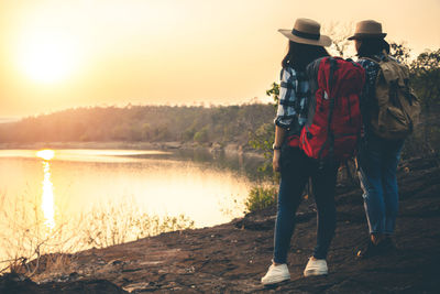 Rear view of men standing on lake against sky during sunset