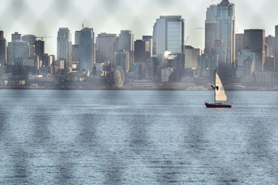 Sailboats in sea against modern buildings in city