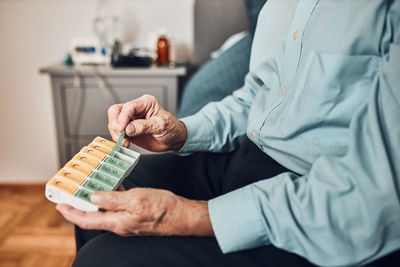 Senior man patient opening pill dispenser to take next medicine dose. organising medication