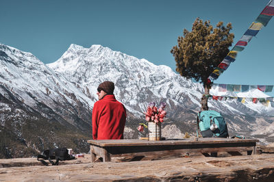 Rear view of man sitting against snowcapped mountains
