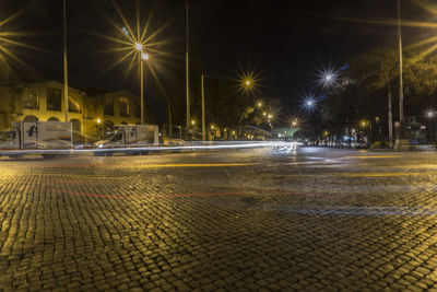 Illuminated street by city against sky at night
