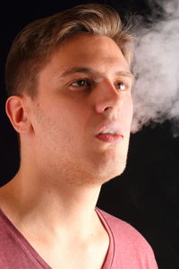 Close-up of young man exhaling smoke against black background