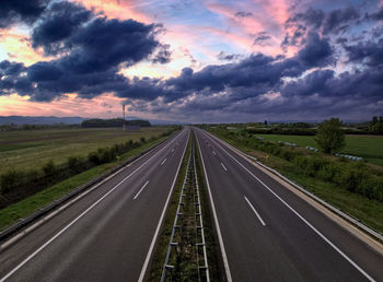 Empty motorway, vanishing point, dramatic sunset sky.