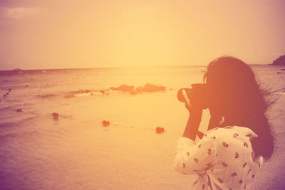 Rear view of woman photographing on beach