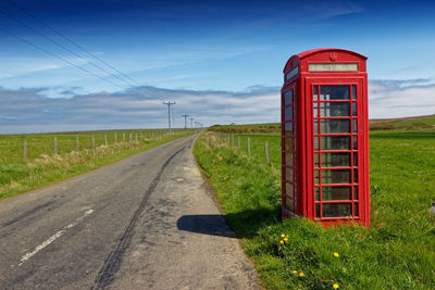 Telephone booth by empty road against sky