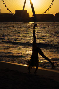 Silhouette of woman doing cartwheel at sunset