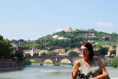 Man wearing sunglasses against river in city against sky