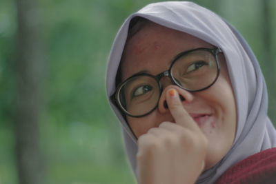 Close-up of smiling young woman wearing eyeglasses and hijab while looking away outdoors