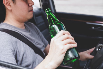Midsection of man holding beer bottle in car