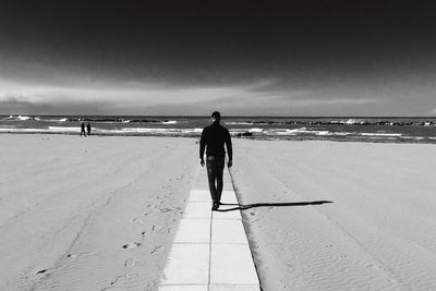 Rear view of man walking at beach against sky