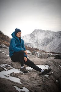 Young tourist in a blue down jacket sits and enjoys the view of the norwegian sea