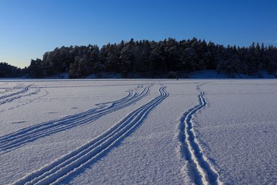 Tire tracks on snow covered field against clear sky