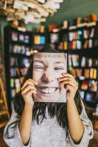 Girl holding book in front of face in bookstore