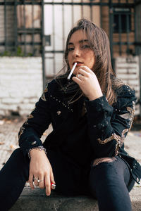 Portrait of young woman smoking cigarette while sitting on land