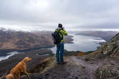 Rear view of woman standing with dog on cliff against valley