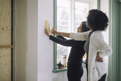 Female customer and architect choosing wall paint color while standing near window at under construction apartment