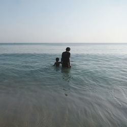 Rear view of man and boy in sea against clear sky