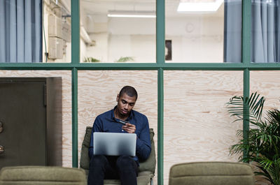 Businessman shopping online with credit card through laptop while sitting at creative office