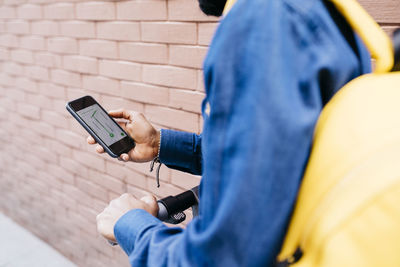 Man with backpack and e-scooter using navigation app on his mobile phone, partial view