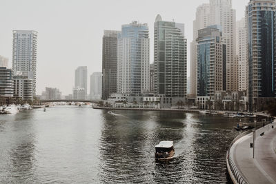 Buildings by river against sky in city