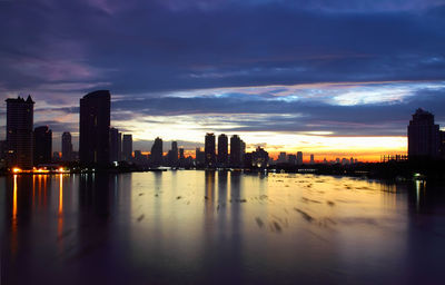 Scenic view of river by buildings against sky during sunset