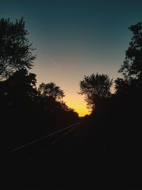 Silhouette trees by road against sky during sunset