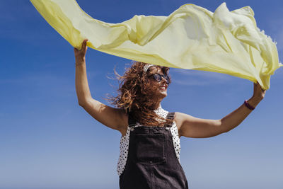 Woman with arms raised standing against sky