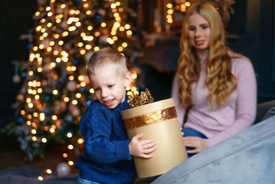 Happy boy received large gift box from his mother, sitting on sofa by christmas