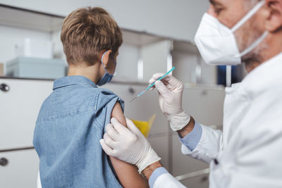 Healthcare worker administering boy with covid-19 vaccine at vaccination center