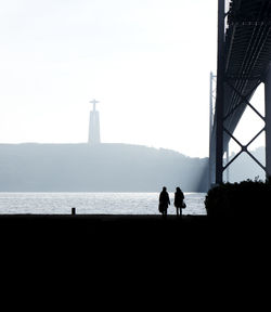 Friends walking at riverbank by april 25th bridge against christ the king statue