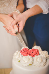 Midsection of bride and groom cutting wedding cake