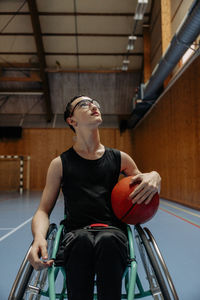 Girl looking up while sitting on wheelchair with basketball at sports court