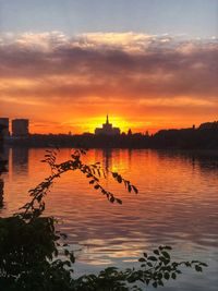 Scenic view of lake by buildings against sky during sunset