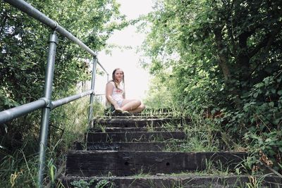 Full length portrait of young woman sitting on land in forest