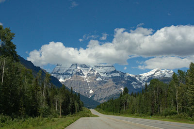 Road amidst trees and mountains against sky