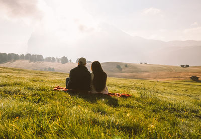 Couple sitting on field against sky