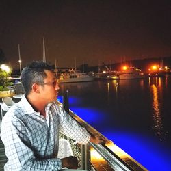 Man sitting in illuminated city against sky at night